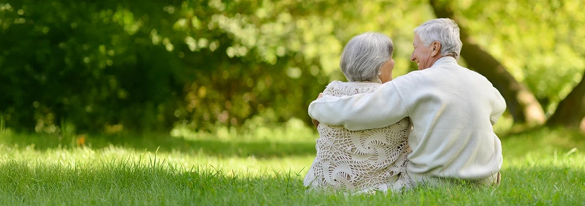 A senior man and woman sit outside in the grass. 